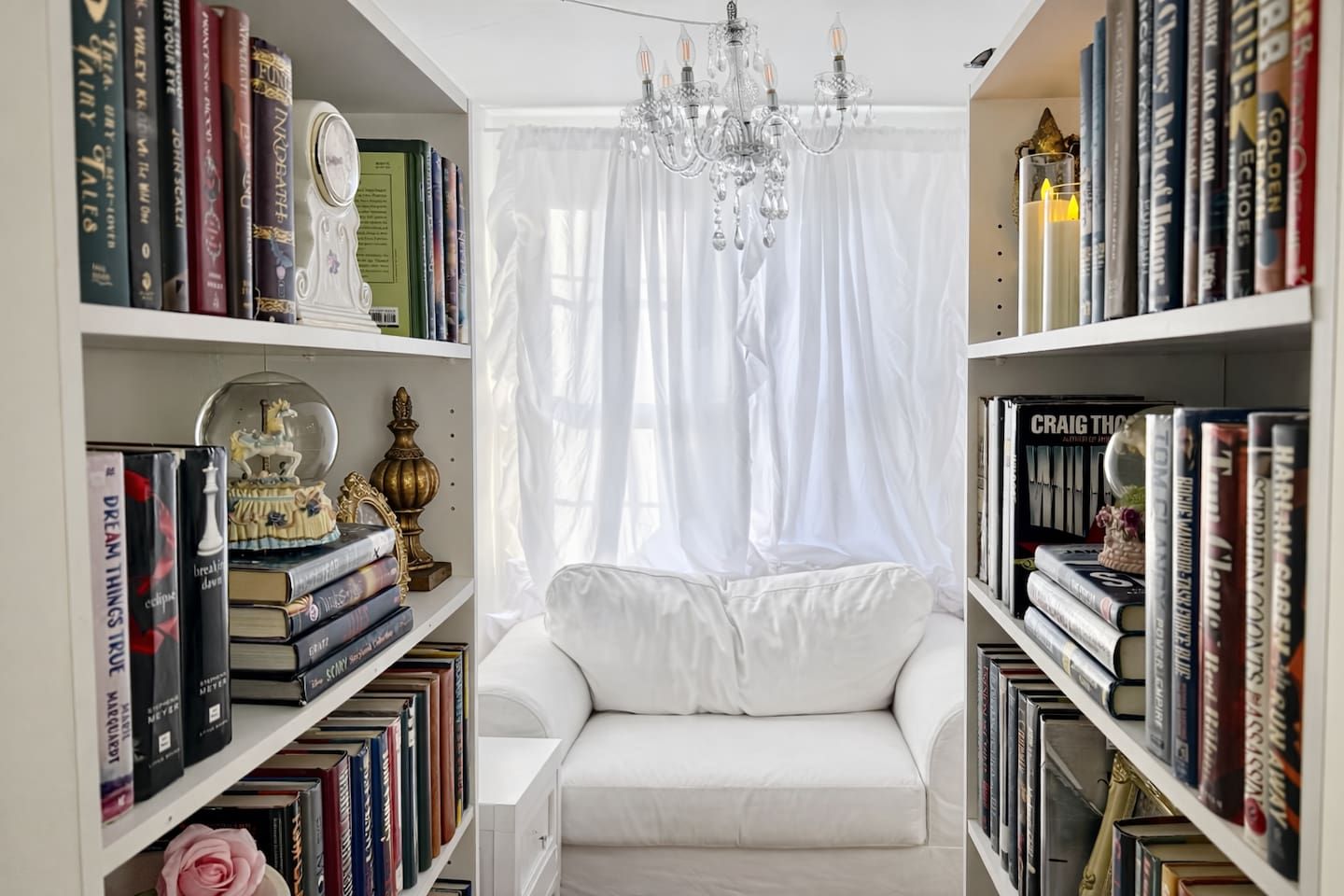 Ein Zimmer mit einem weißen Sofa, einer Chandelüster und Bücherregalen voller Bücher.