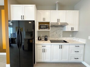 A modern kitchen with white cabinetry, a black refrigerator, a microwave, and a stove. - 5704- Cozy 2B1B Private Unit near FWY 580/24 & UCB (Oakland)