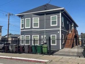 A two-story residential building with a grey exterior, white window frames, and a black metal fence. - 5704- Cozy 2B1B Private Unit near FWY 580/24 & UCB (Oakland)