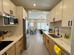 A modern kitchen with white cabinets, stainless steel appliances, and a dining area with a table and chairs. - 5704- Cozy 2B1B Private Unit near FWY 580/24 & UCB (Oakland)