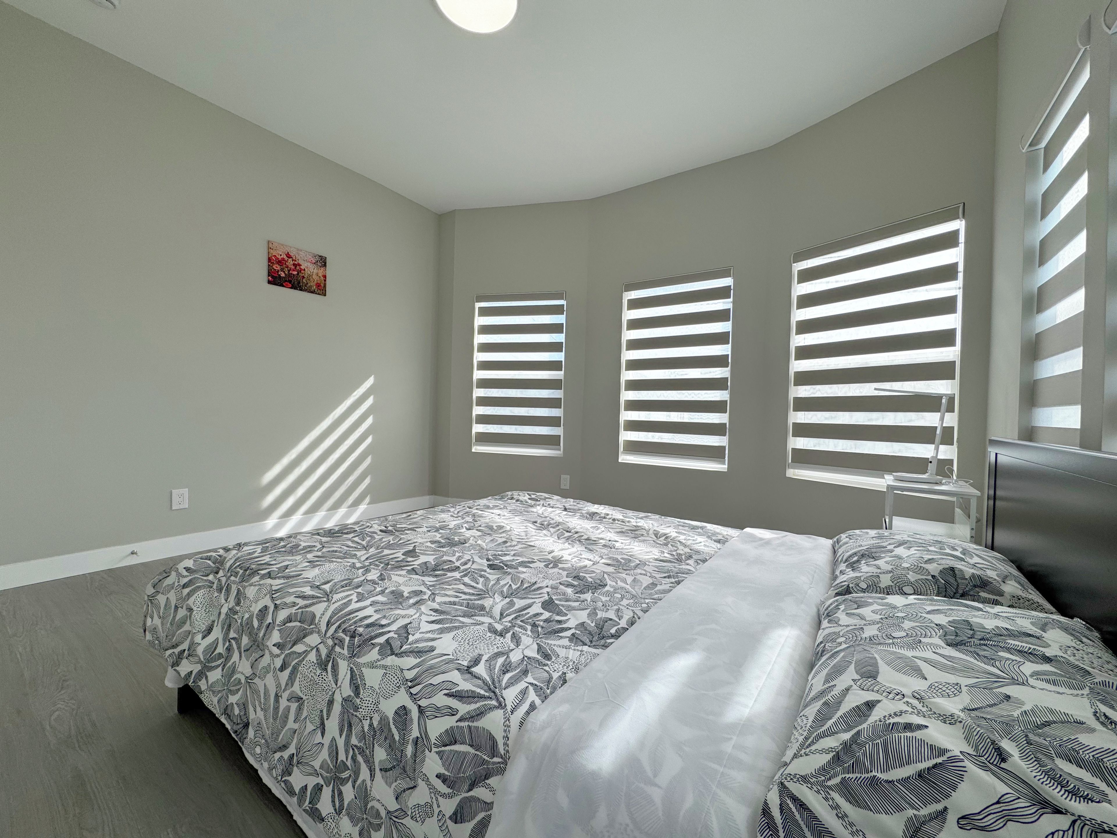 A bedroom with a bed, a desk, and a window with blinds.
