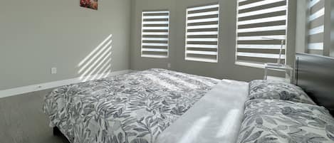 A bedroom with a bed, a desk, and a window with blinds.