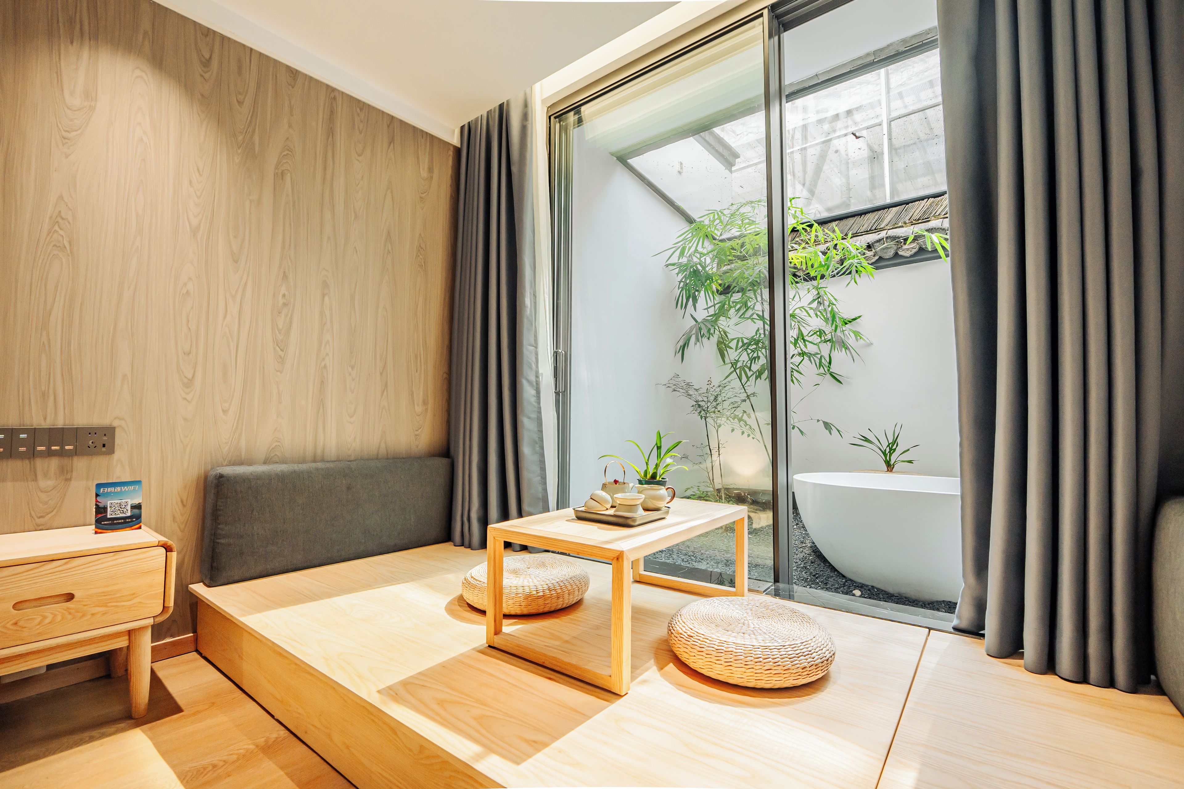 Habitació moderna amb terra de fusta, un sofà, una taula petita i vista a un jardí a través d'una porta de vidre.