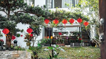 Un jardín con un árbol, faroles rojos y un muro de piedra.