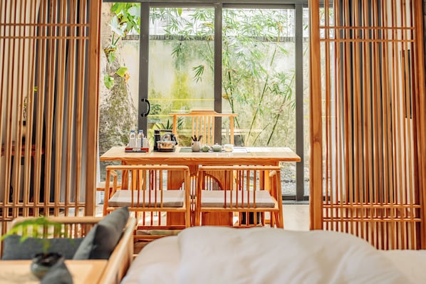 A room with a wooden table, chairs, and a view of greenery outside.