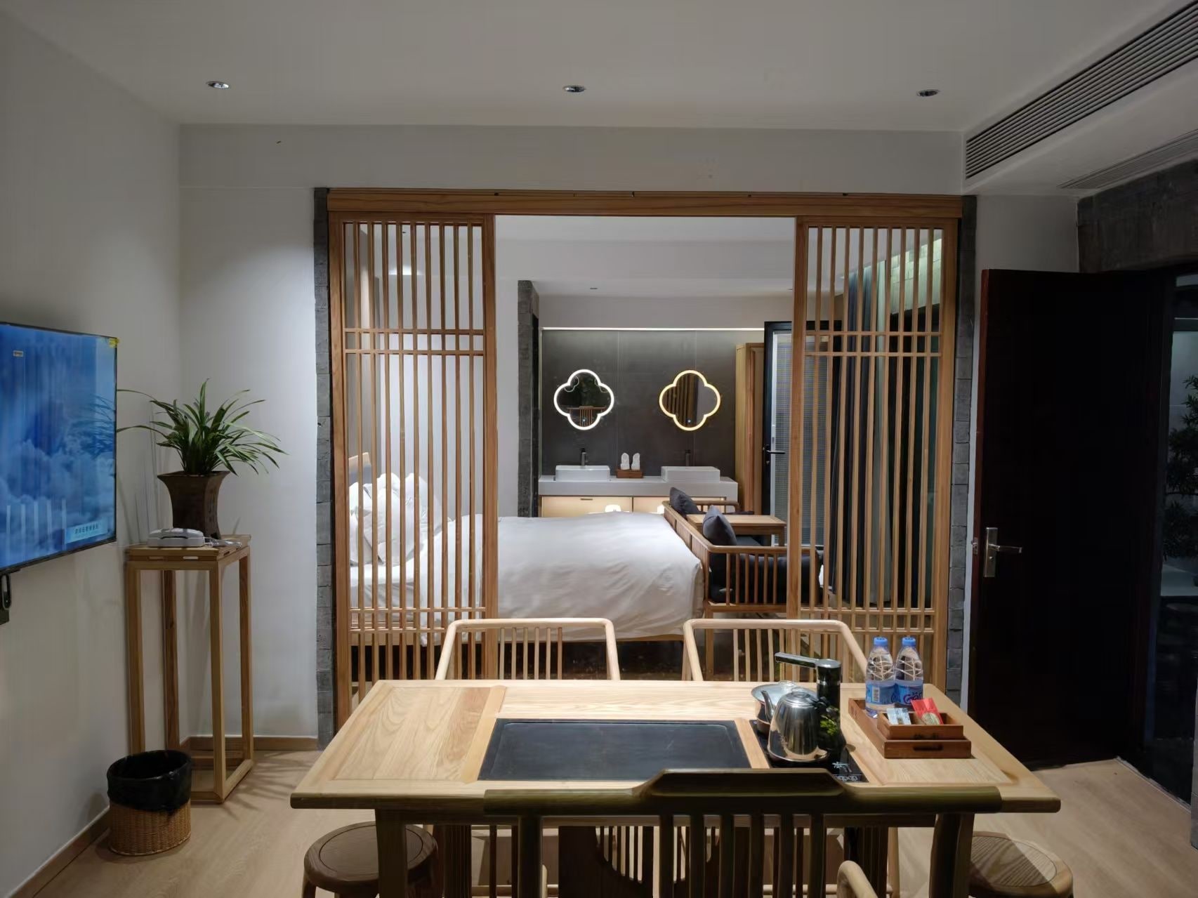 Habitación de hotel moderna con un separador de madera, una cama, un escritorio y vista al baño.