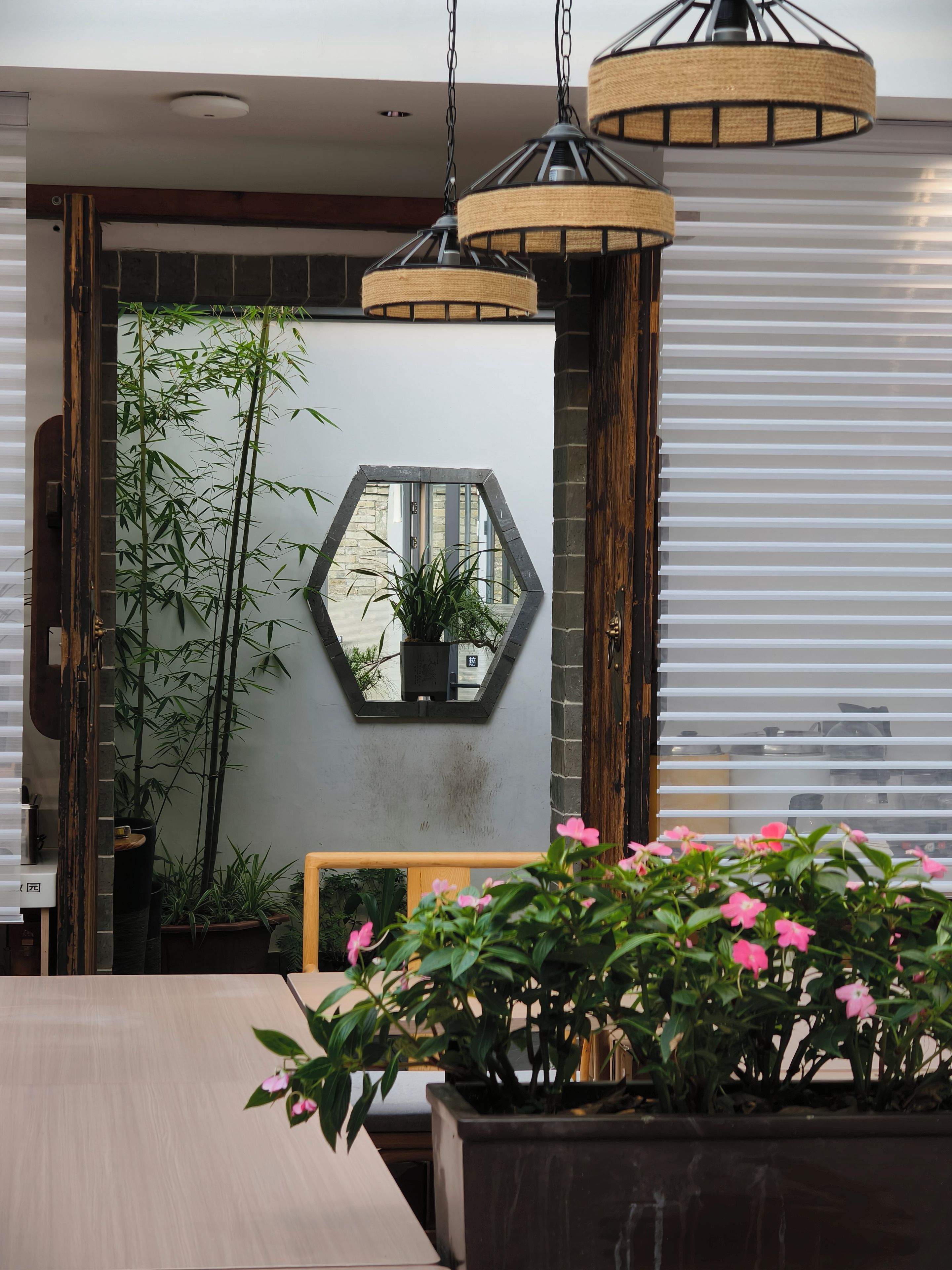 A modern interior with a hexagonal mirror, bamboo plants, and a wooden table.