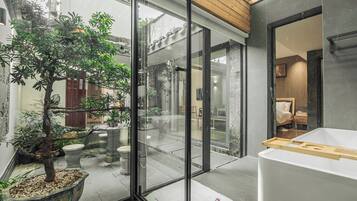 Un interior moderno con una puerta de vidrio que da a un patio con un árbol y plantas en macetas.