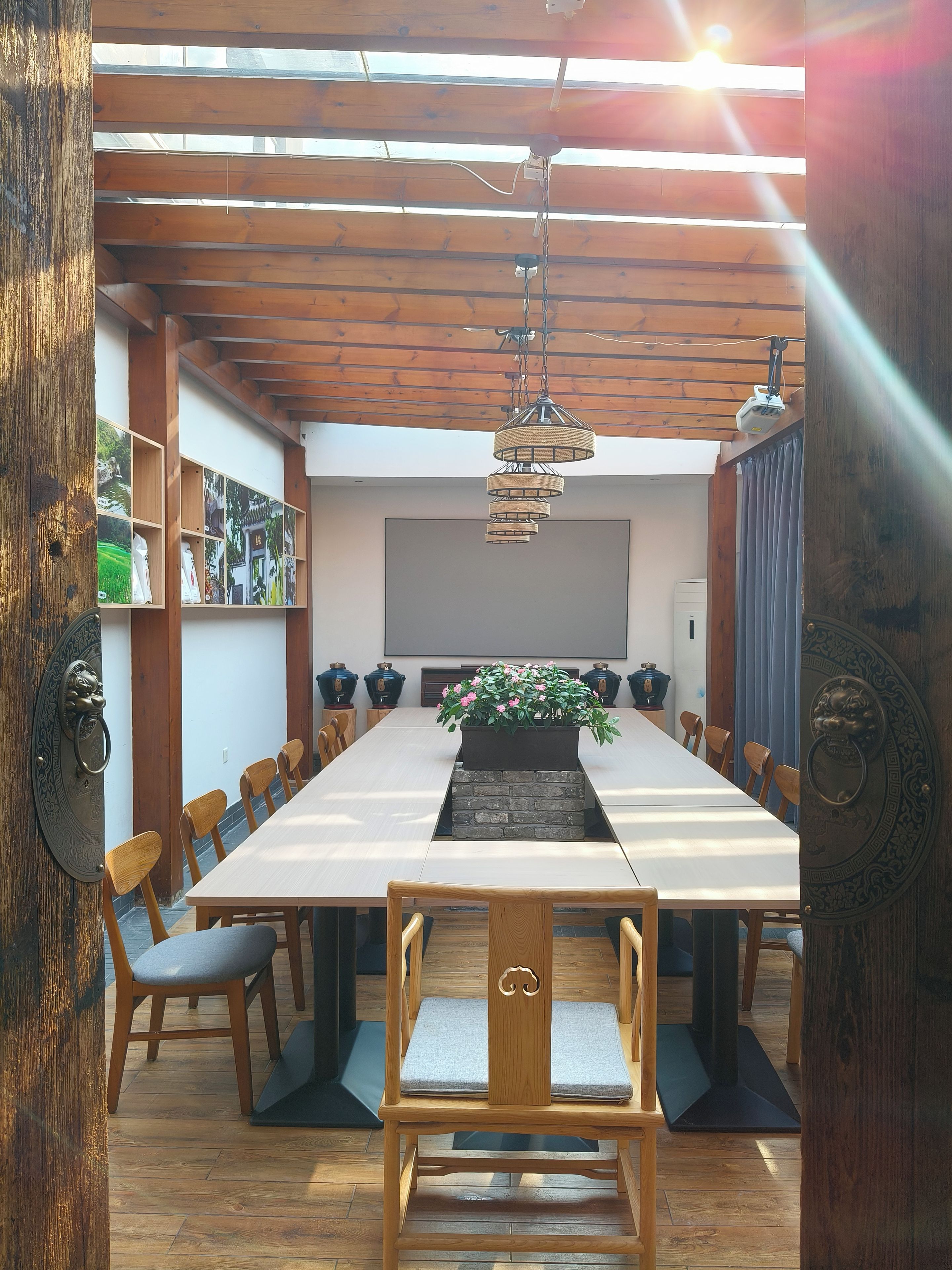 Un comedor con una mesa larga, sillas, una lámpara colgante y una planta en maceta.