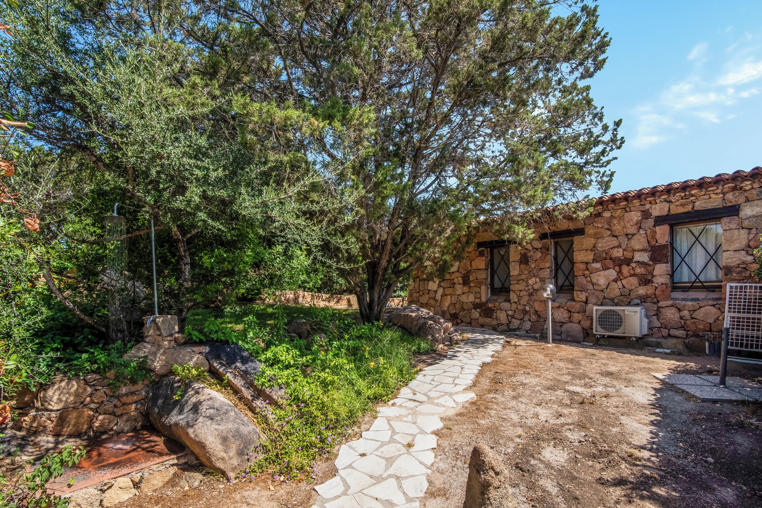 A stone building with a stone pathway leading to it, surrounded by greenery and trees.