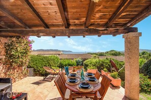 An outdoor patio with a wooden pergola, a table set for dining, and a view of the sea and hills in the background. - Casa Molara, Punta Molara, Italy (Punta Molara)
