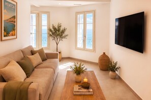 A living room with a sofa, a coffee table with books and candles, a TV, and large windows with a view. - Horizon azur, Menton, France (Menton)