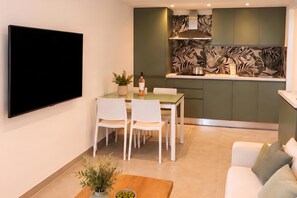 Um espaço de estar compacto com TV de tela plana, área de jantar com cadeiras, cozinha com design moderno e um sofá.