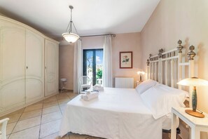 A hotel room with a bed, a chair, a table, a radiator, and a window with curtains. - Masseria Saracino Pool And Garden, Martano, Italy (Martano)