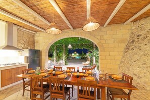 Un espace de restauration en plein air agrémenté d’une arche en pierre, de mobilier en bois et de luminaires suspendus.
