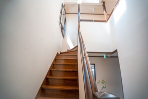Eine Holztreppe mit Handlauf, die zu einer Zwischenebene mit einer Tür und einer kleinen Pflanze führt.