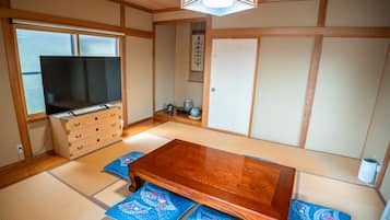 A traditional Japanese room with tatami flooring, a wooden table, a television, and a sliding door.