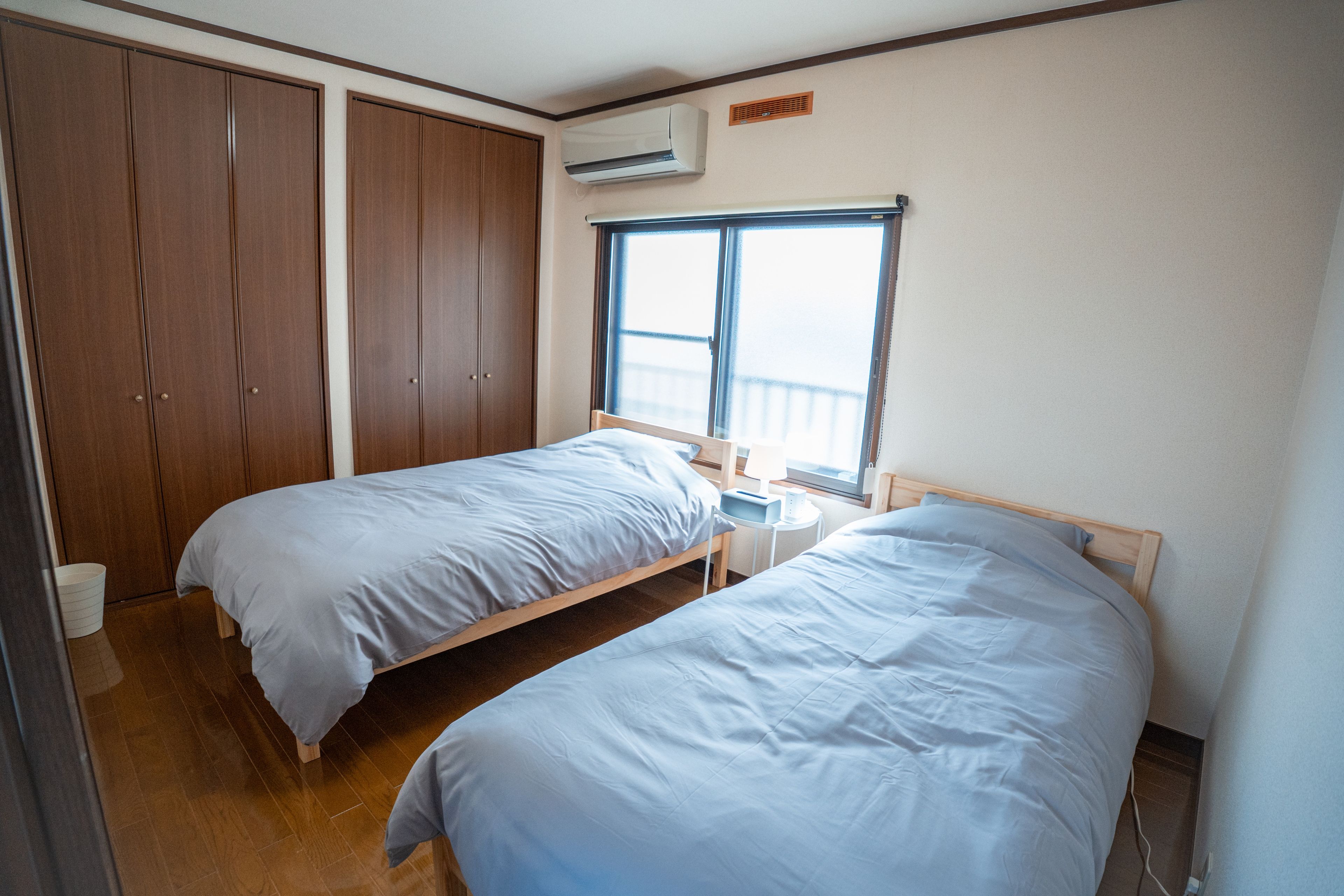 A bedroom with two single beds, a wardrobe, an air conditioning unit, and a window.