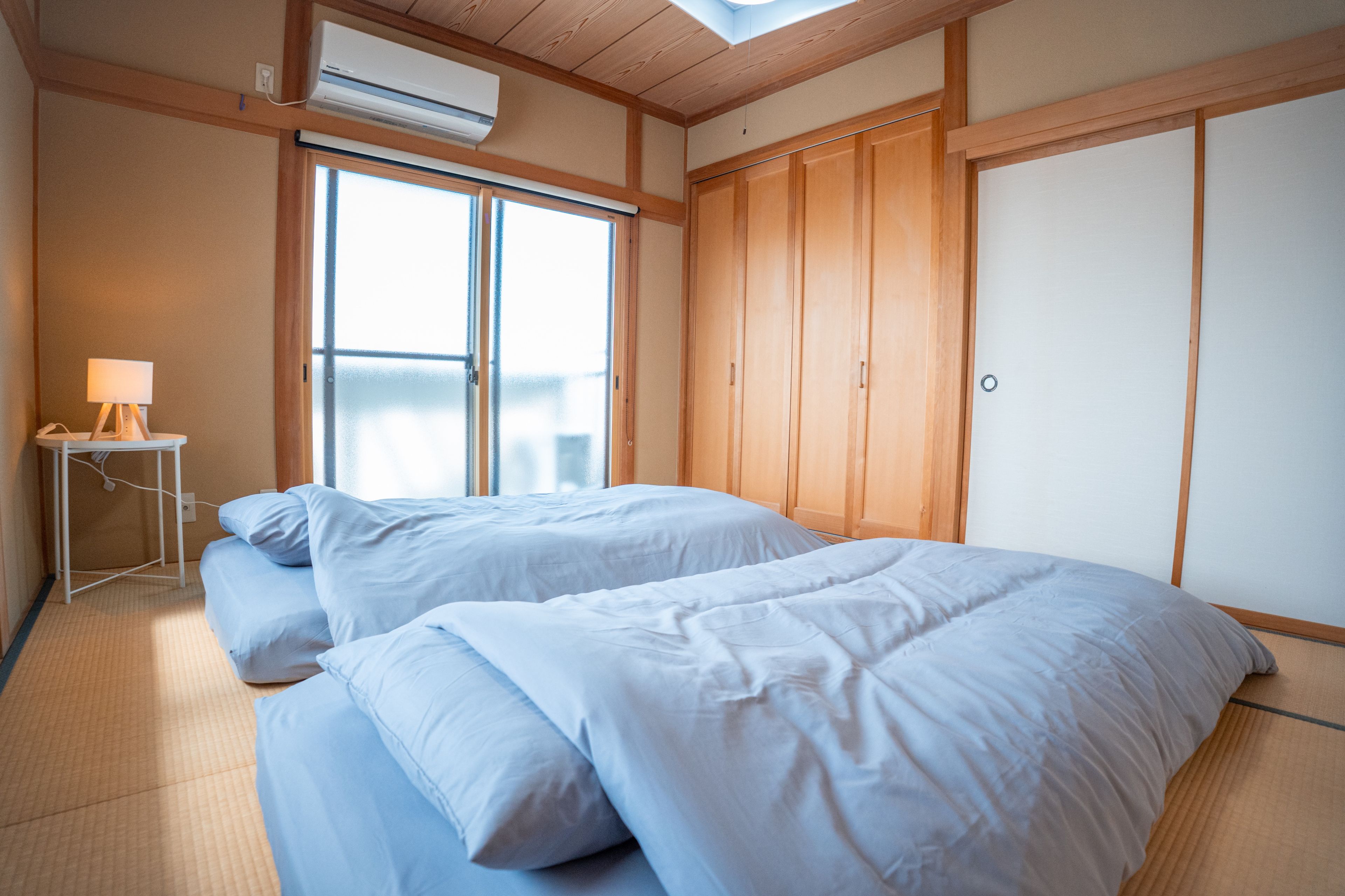A room with two beds, a small table with a lamp, and a wardrobe.