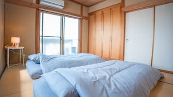 A room with two beds, a small table with a lamp, and a wardrobe.