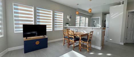 A modern living room with a flat-screen TV, dining table, and chairs.