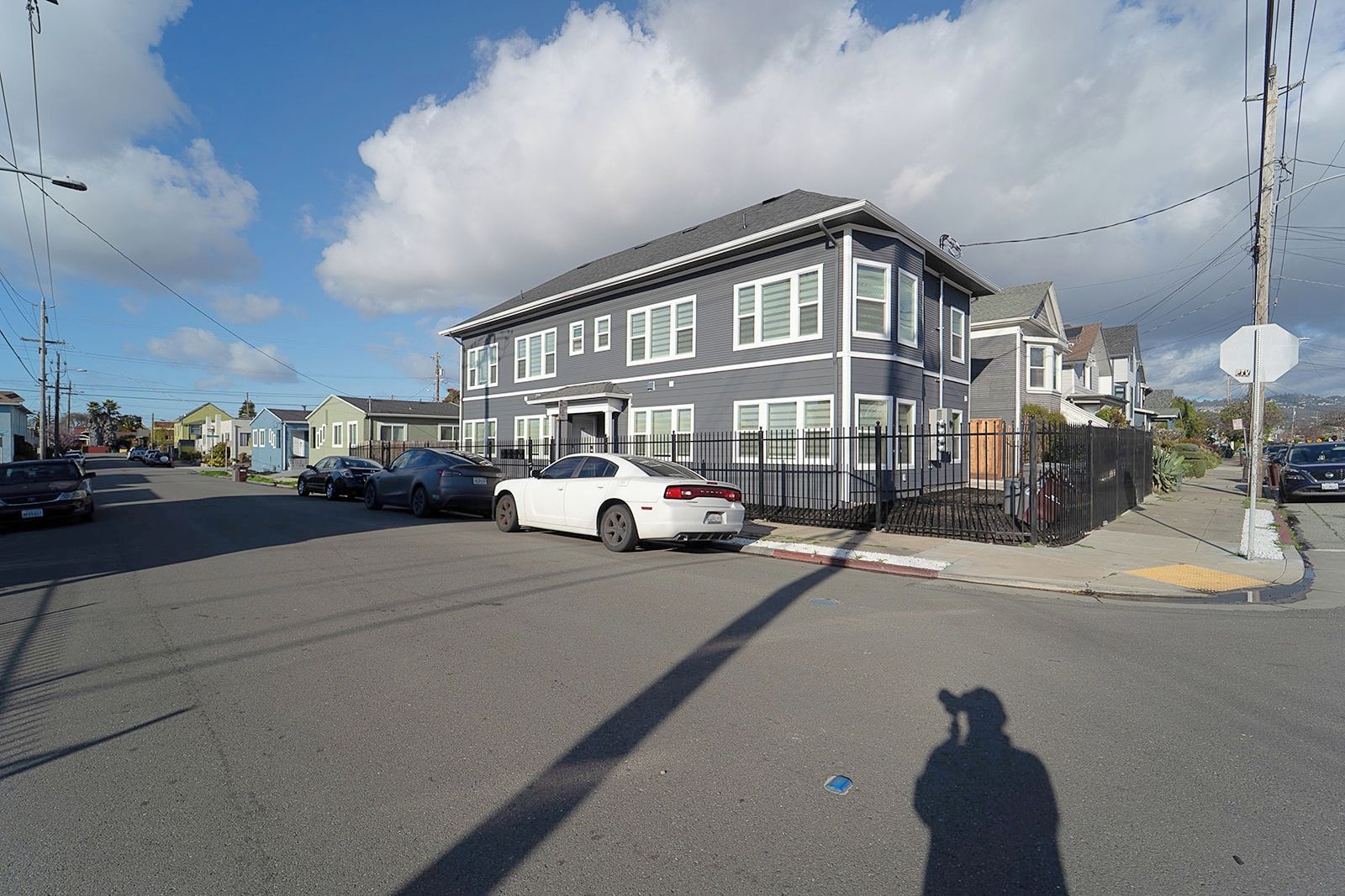 A residential street with a two-story house, parked cars, and a clear sky.