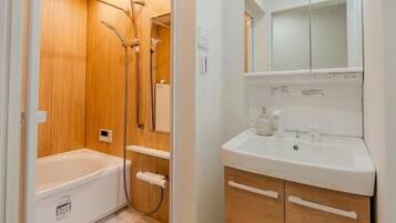A compact bathroom with a bathtub, a shower, a sink, and a mirror.