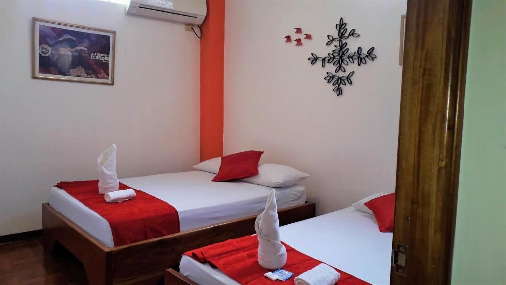 Habitación de hotel con dos camas, cada una con una manta roja y almohada blanca, y una decoración en la pared.