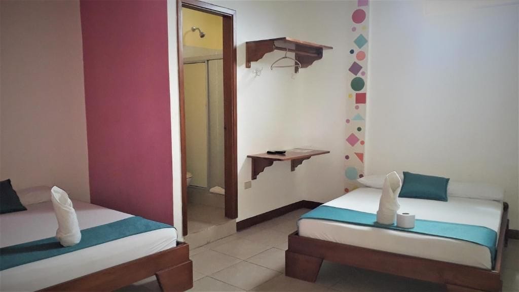 Ein Hotelzimmer mit zwei Betten, einem Spiegel, einer Holzablage und einer Tür zu einem weiteren Raum.