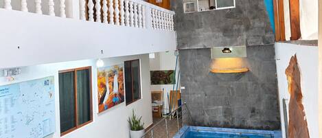 A multi-level indoor space with a swimming pool, a balcony with a railing, and a wall with a map and artwork.