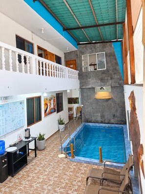 Un espacio interior de varios niveles con una piscina, un balcón con barandilla y una pared con un mapa y obras de arte.