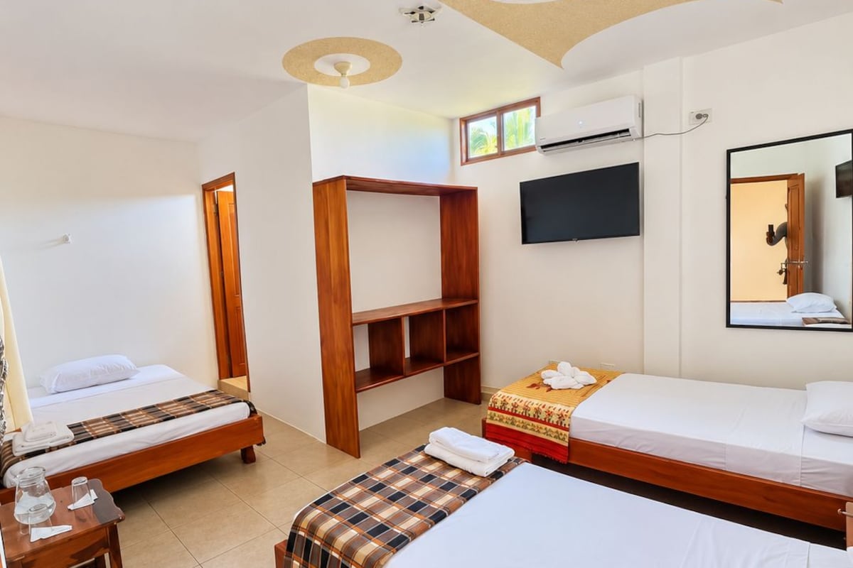 Una habitación de hotel con dos camas, un armario de madera, un televisor y un ventilador de techo.
