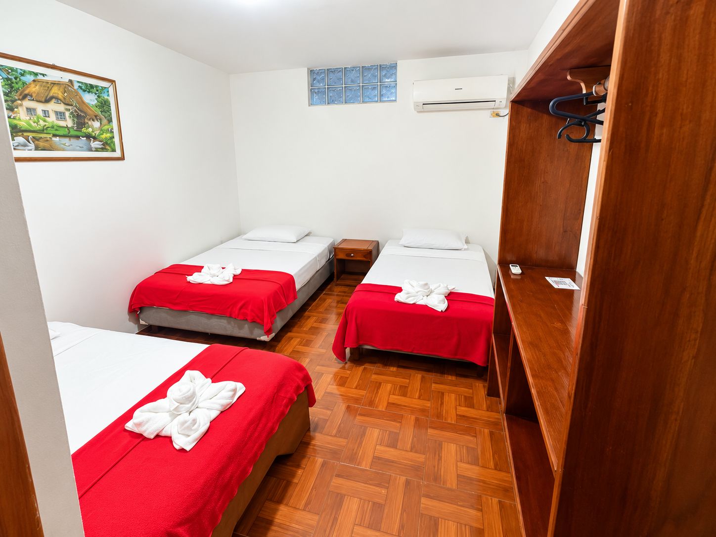 Une chambre d’hôtel avec deux lits, un plancher en bois, un tableau au mur et un appareil de climatisation.