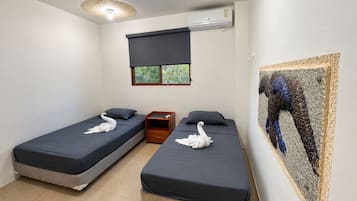 Une chambre avec deux lits simples, une table de chevet, un appareil de climatisation et une fenêtre donnant sur un espace verdoyant.