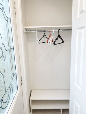 A closet with a white bench and a rod holding three hangers.