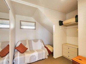 A bedroom with a sloped ceiling, a bed with striped bedding, a dresser, and a window with blinds. - The Heart of Hahei, a modern and central home only steps away from shops / beach (Hahei)