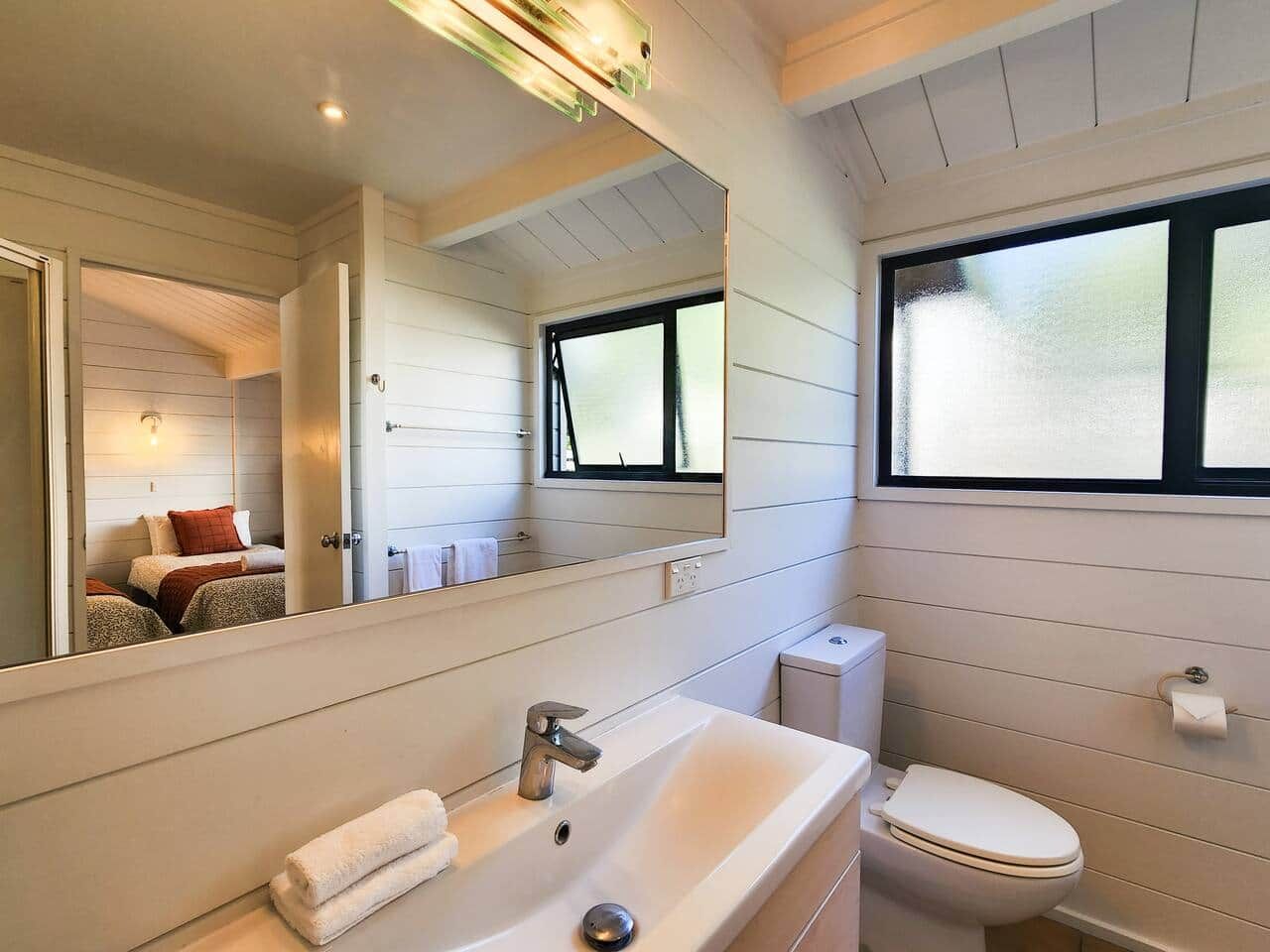 A bathroom with a large mirror, a sink, a toilet, and a window.