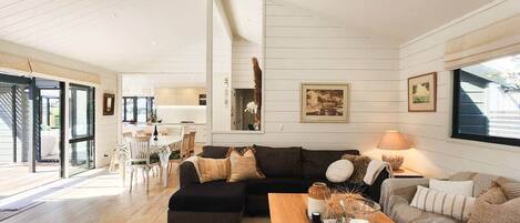 A spacious living area with a large black sectional sofa, a wooden coffee table, and a striped sofa. There is a dining area visible through an open door.