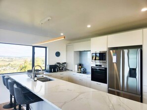 A modern kitchen with a large island, stainless steel appliances, and a view of the countryside. - Tirohanga a Hei - "The view of Hei" Adults only (Hahei)