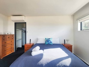 A bedroom with a bed, a dresser, a nightstand, a window, and an air conditioning unit. - Tirohanga a Hei - "The view of Hei" Adults only (Hahei)