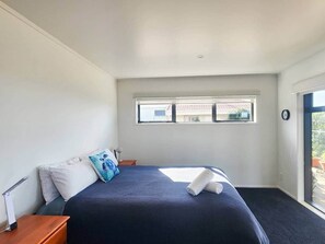 A bedroom with a bed, a nightstand, a window, and a door leading to an outdoor area. - Tirohanga a Hei - "The view of Hei" Adults only (Hahei)