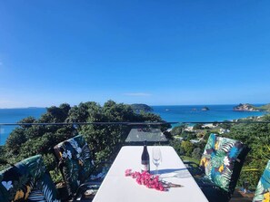 A terrace with a table set for two, overlooking a coastal landscape. - Tirohanga a Hei - "The view of Hei" Adults only (Hahei)