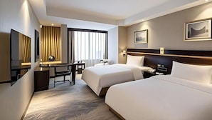 Habitación de hotel con dos camas, un escritorio, una silla, un televisor y una ventana con cortinas.