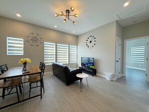 A modern living room with a dining table, sofa, TV, and decorative wall clock. - 5710- Safe 2B1B Private Unit near FWY 580/24 & UCB (Oakland)