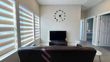 A living room with a black leather sofa, a flat-screen TV on a stand, and a wall clock.