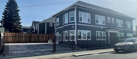 A two-story residential building with a black exterior and white trim, a gated driveway, and a parked car.