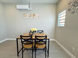 A dining area with a wooden table and four chairs, a vase with flowers, and a wall-mounted air conditioner. - 5710- Safe 2B1B Private Unit near FWY 580/24 & UCB (Oakland)