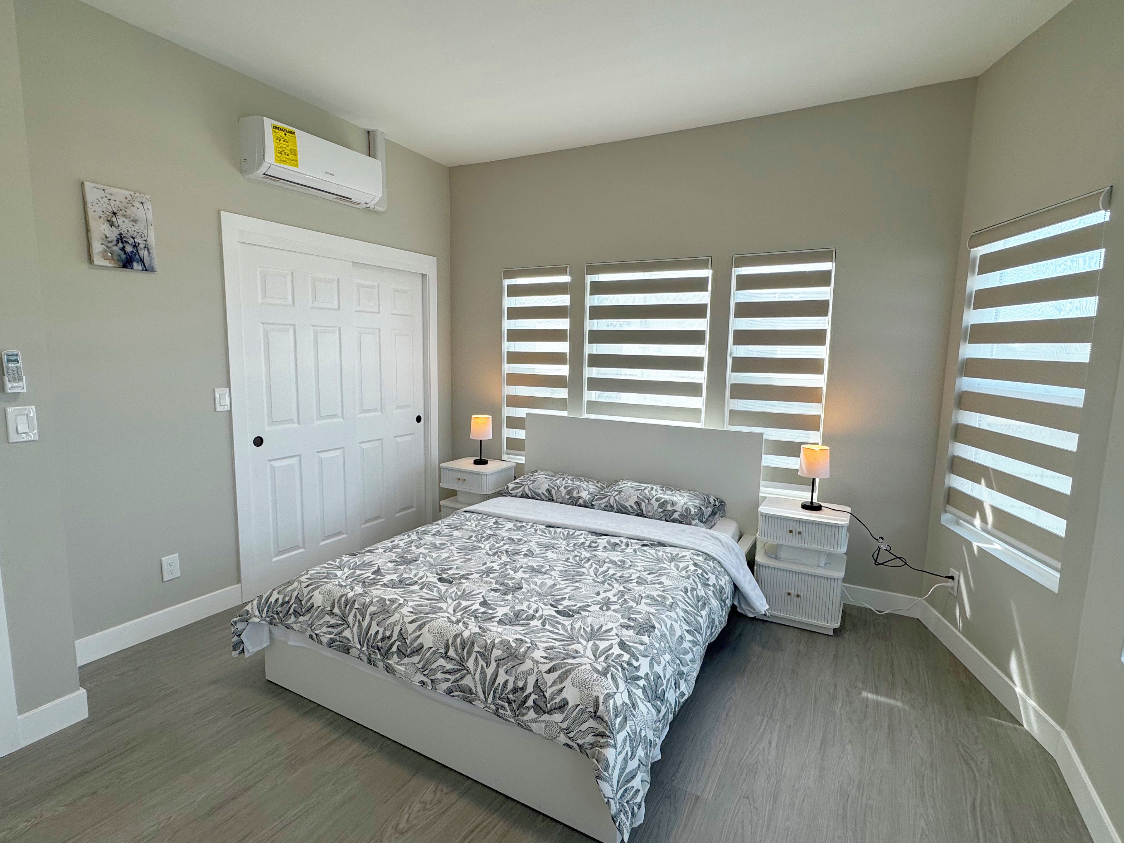 A bedroom with a bed, bedside tables, a door, and a window with blinds.