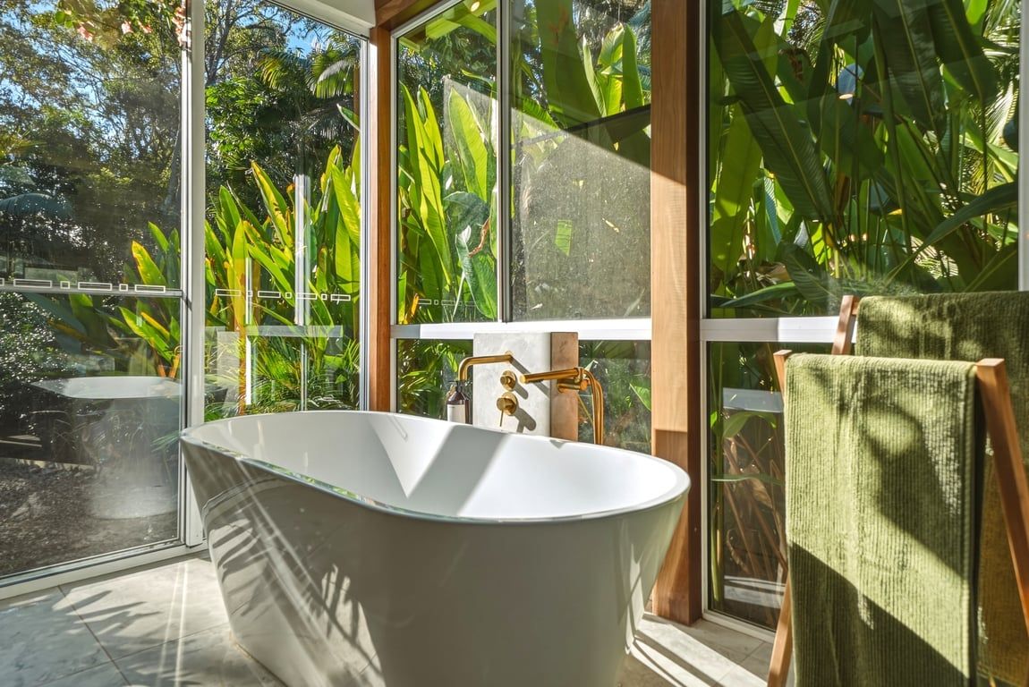 A modern bathroom with a freestanding bathtub, large windows, and a view of lush greenery.