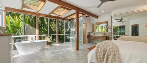 A spacious bedroom with a large bed, a bathtub, and a balcony with glass doors.